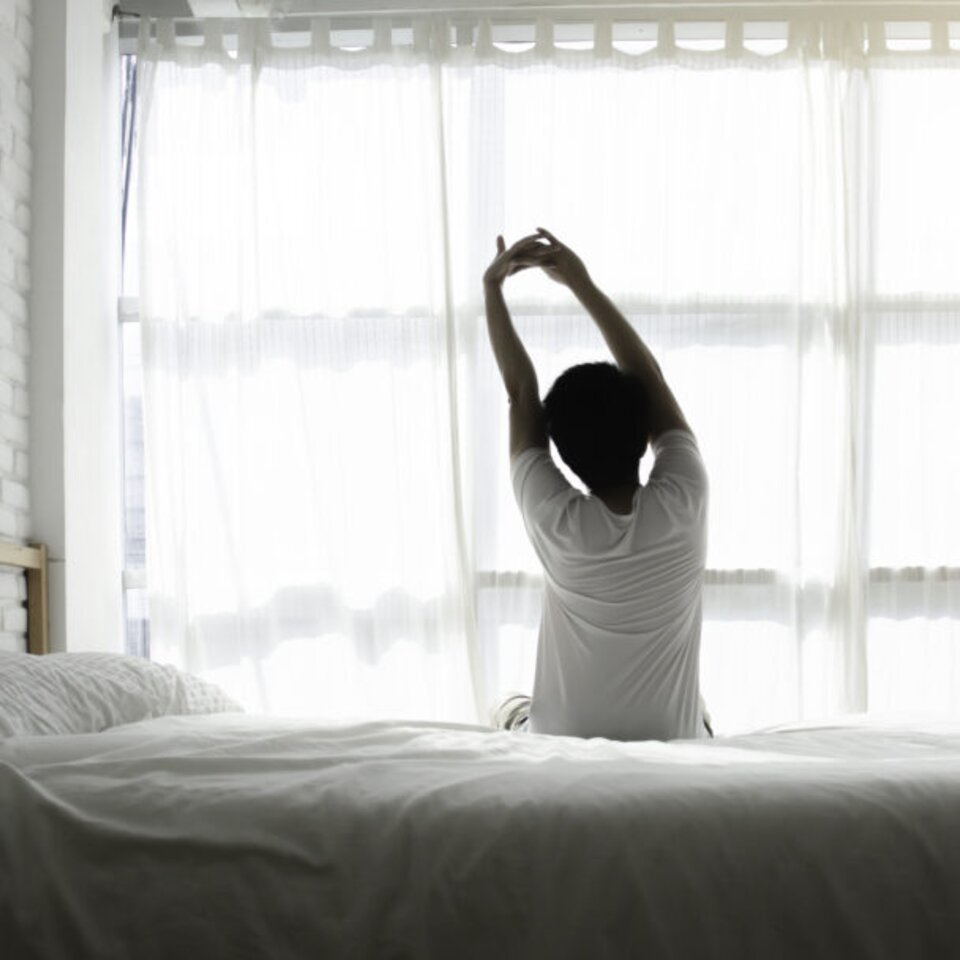 Men sit at the edge of the bed. And stretching his arms to relax in the morning.Wake up in the morning.Stretching after waking.