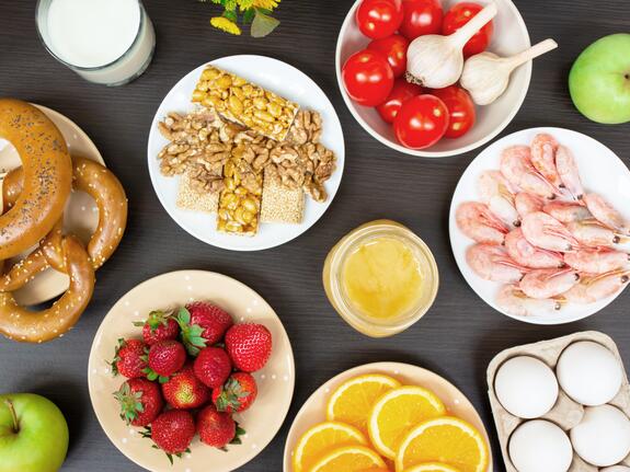Various foods such as strawberries, shrimps, nuts, tomatoes, eggs and honey on plates