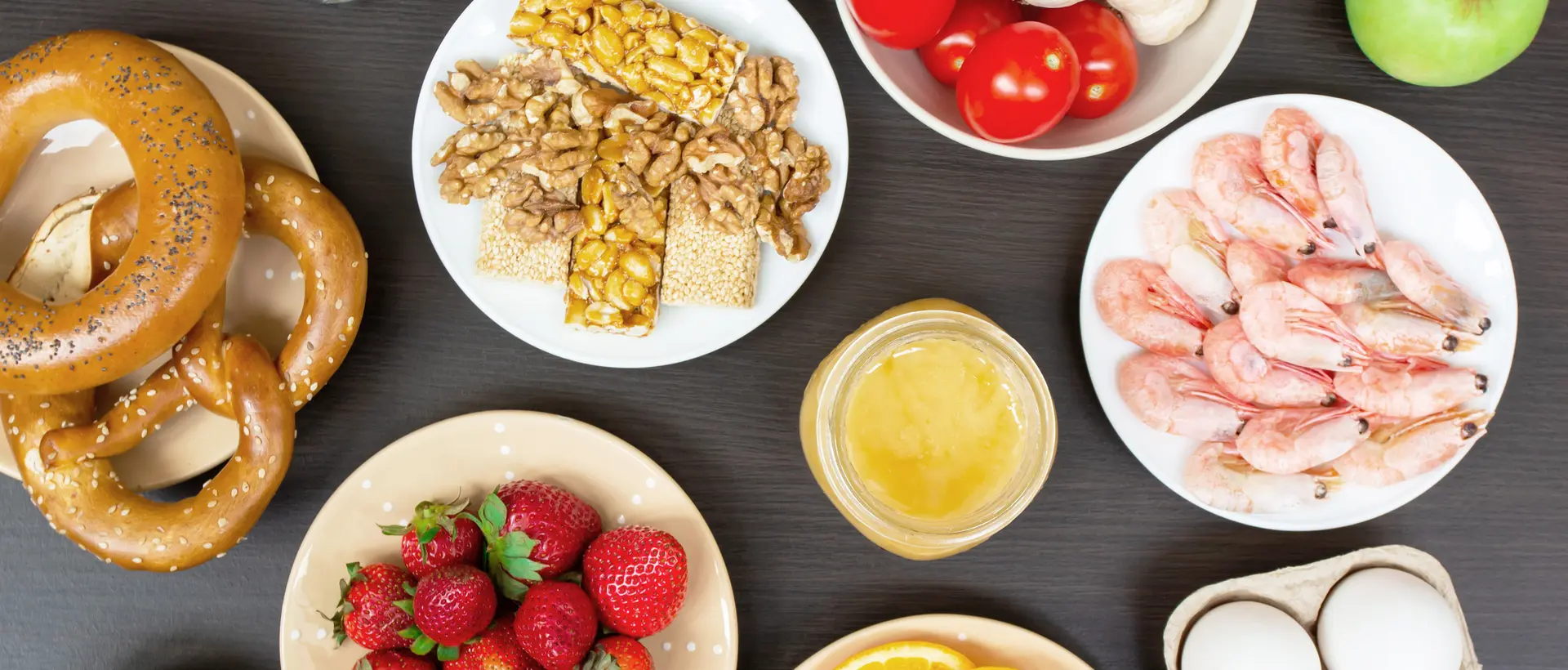 Various foods such as strawberries, shrimps, nuts, tomatoes, eggs and honey on plates