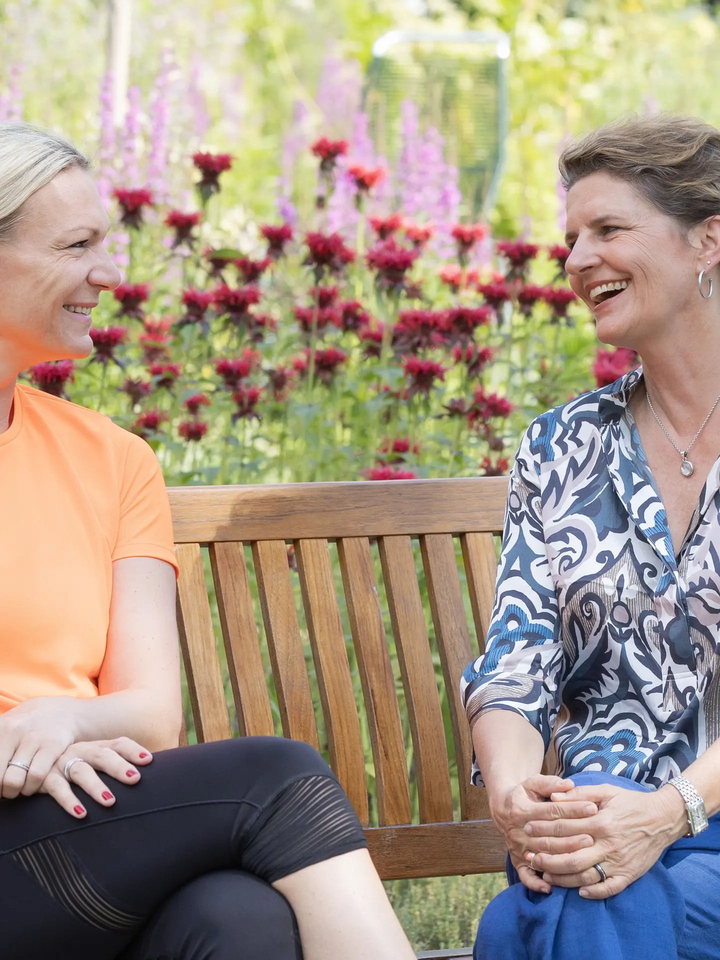 Maria Höfl-Riesch and Managing Director Andrea Gnägi chatting and laughing on a park bench in the garden at Park Igls