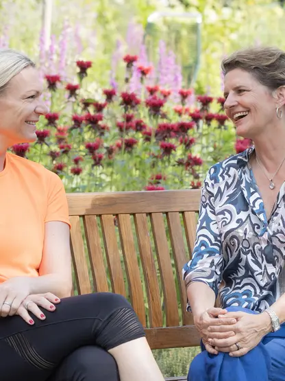 Maria Höfl-Riesch and Managing Director Andrea Gnägi chatting and laughing on a park bench in the garden at Park Igls