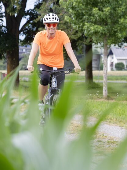 Maria Höfl-Riesch cycling through lush green landscape on a mountain bike with helmet