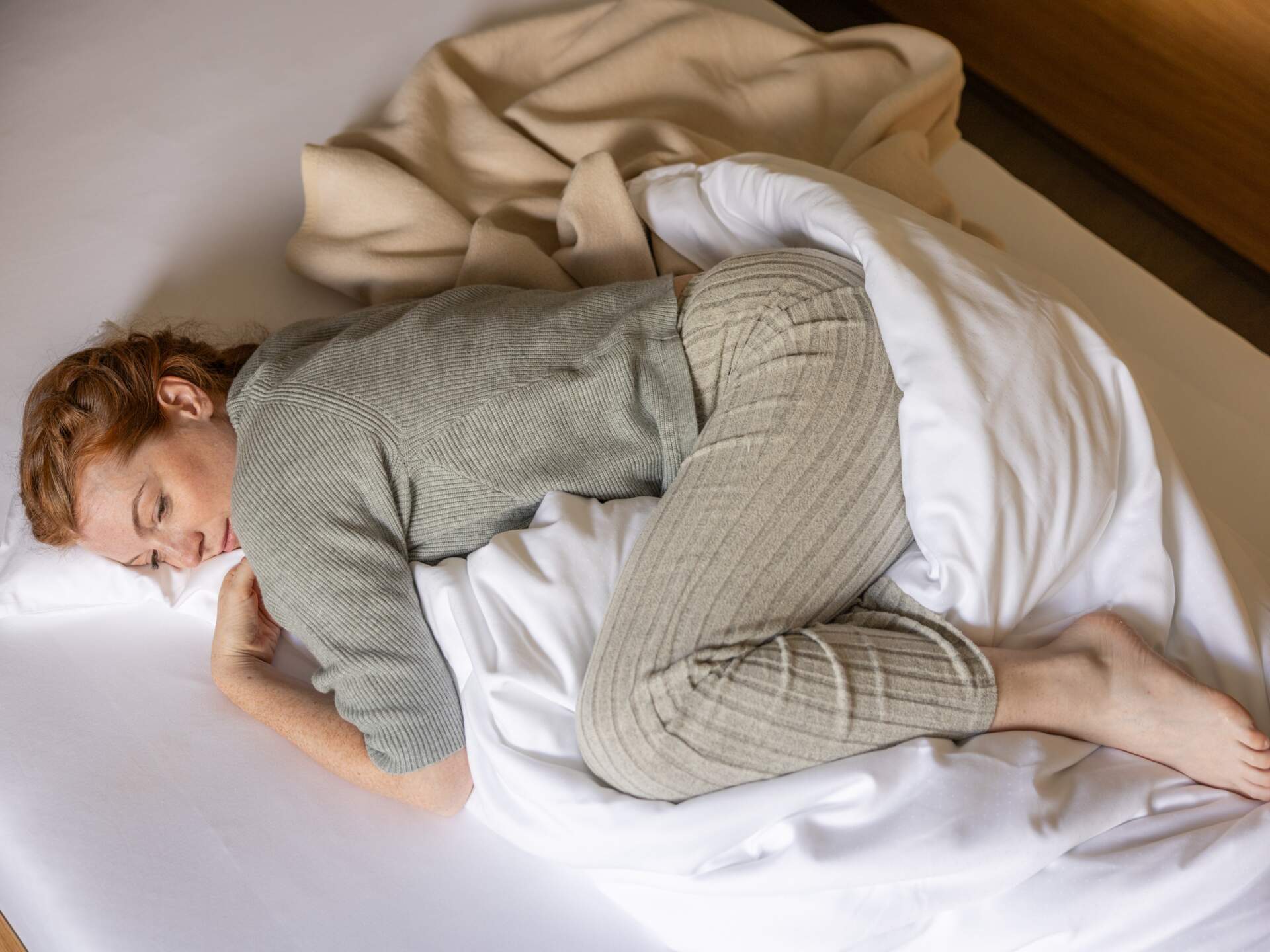 Frau in Loungewear zusammengerollt im Bett – Rückzug und Ruhe bei Regelschmerzen
