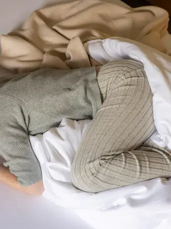 Frau in Loungewear zusammengerollt im Bett – Rückzug und Ruhe bei Regelschmerzen