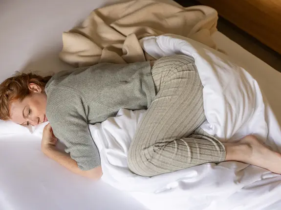 Woman in loungewear curled up in bed – rest and retreat during menstrual discomfort