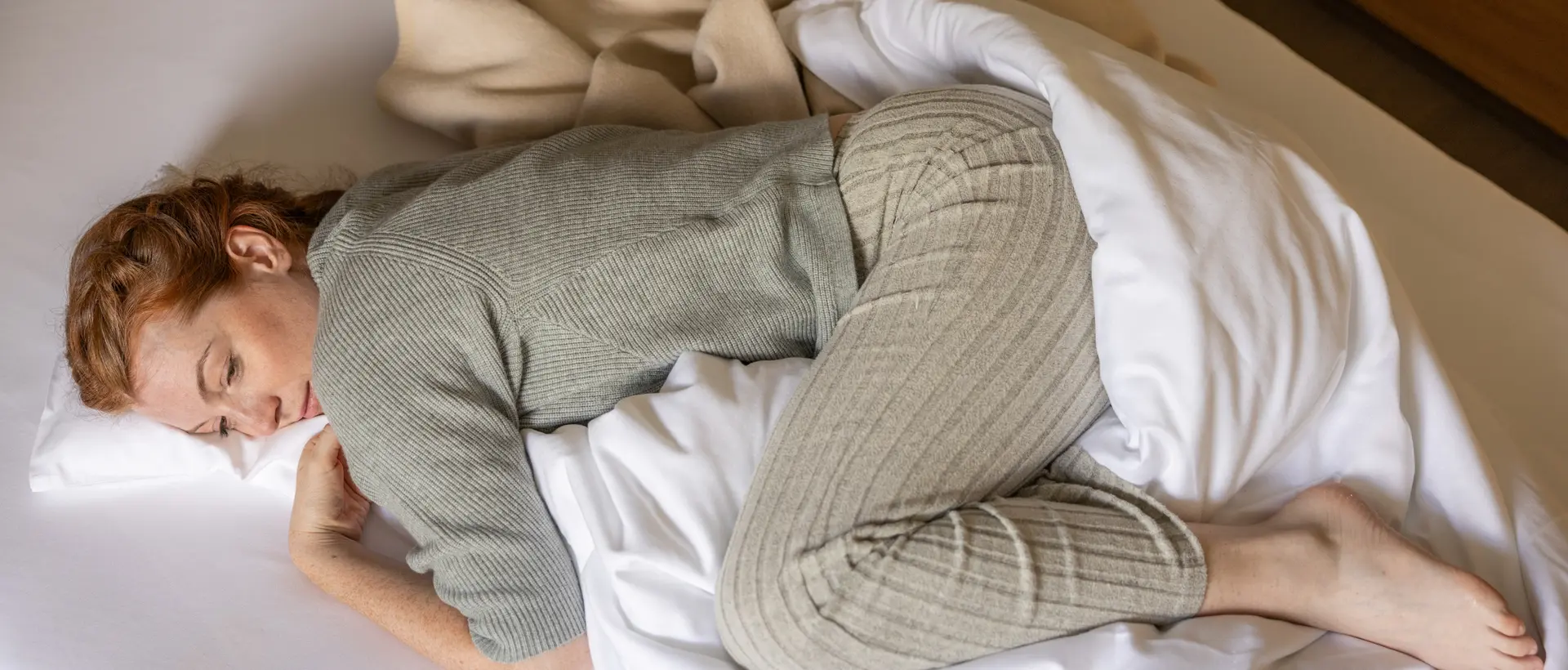 Woman in loungewear curled up in bed – rest and retreat during menstrual discomfort
