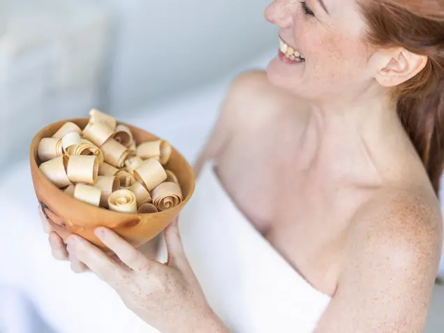 Lächelnde Frau hält eine Schale mit Zirbenspänen – natürliche Düfte für Wohlbefinden und innere Balance
