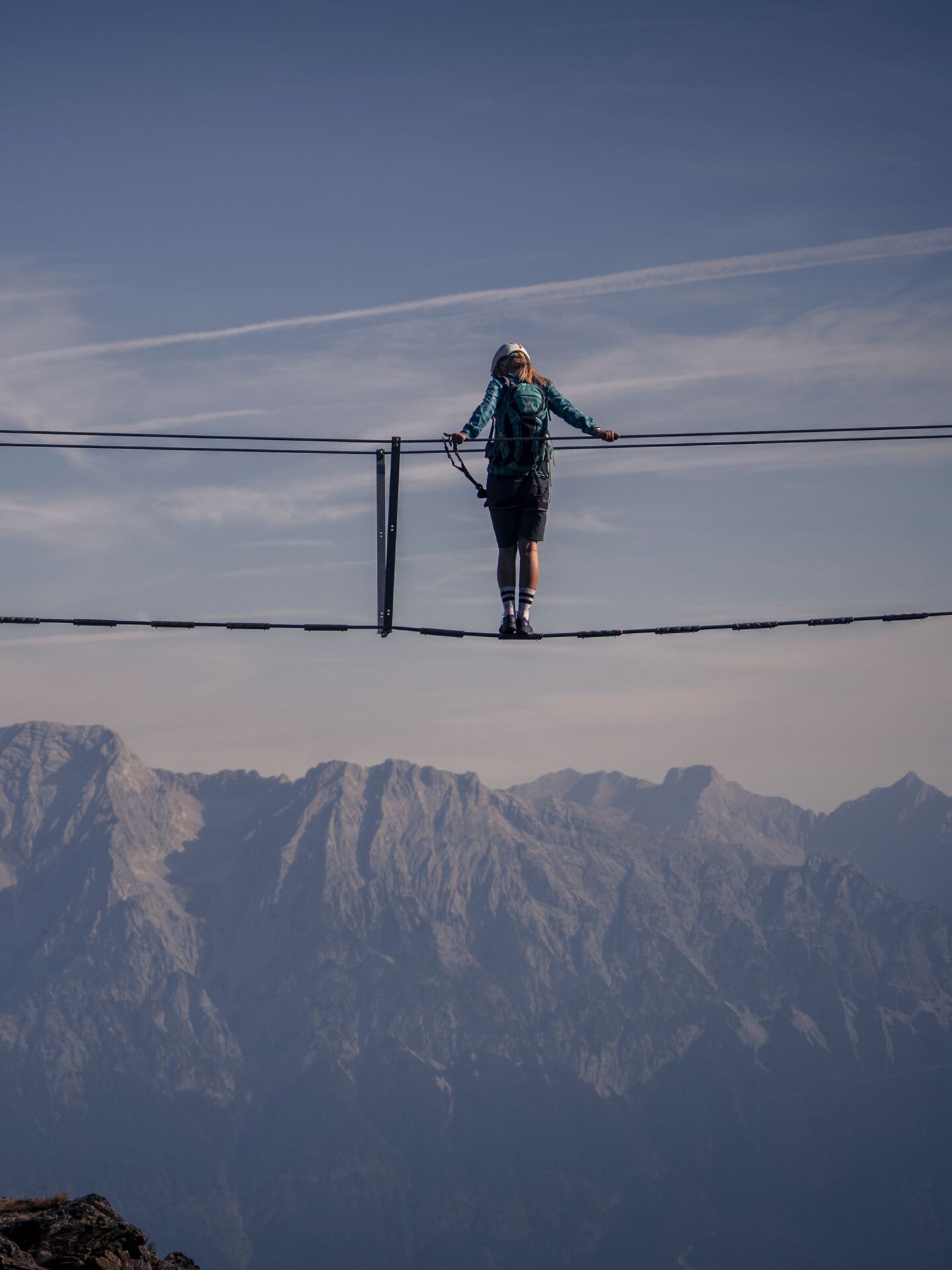 Person on suspension bridge in front of mountain panorama on the Glungezer via ferrata
