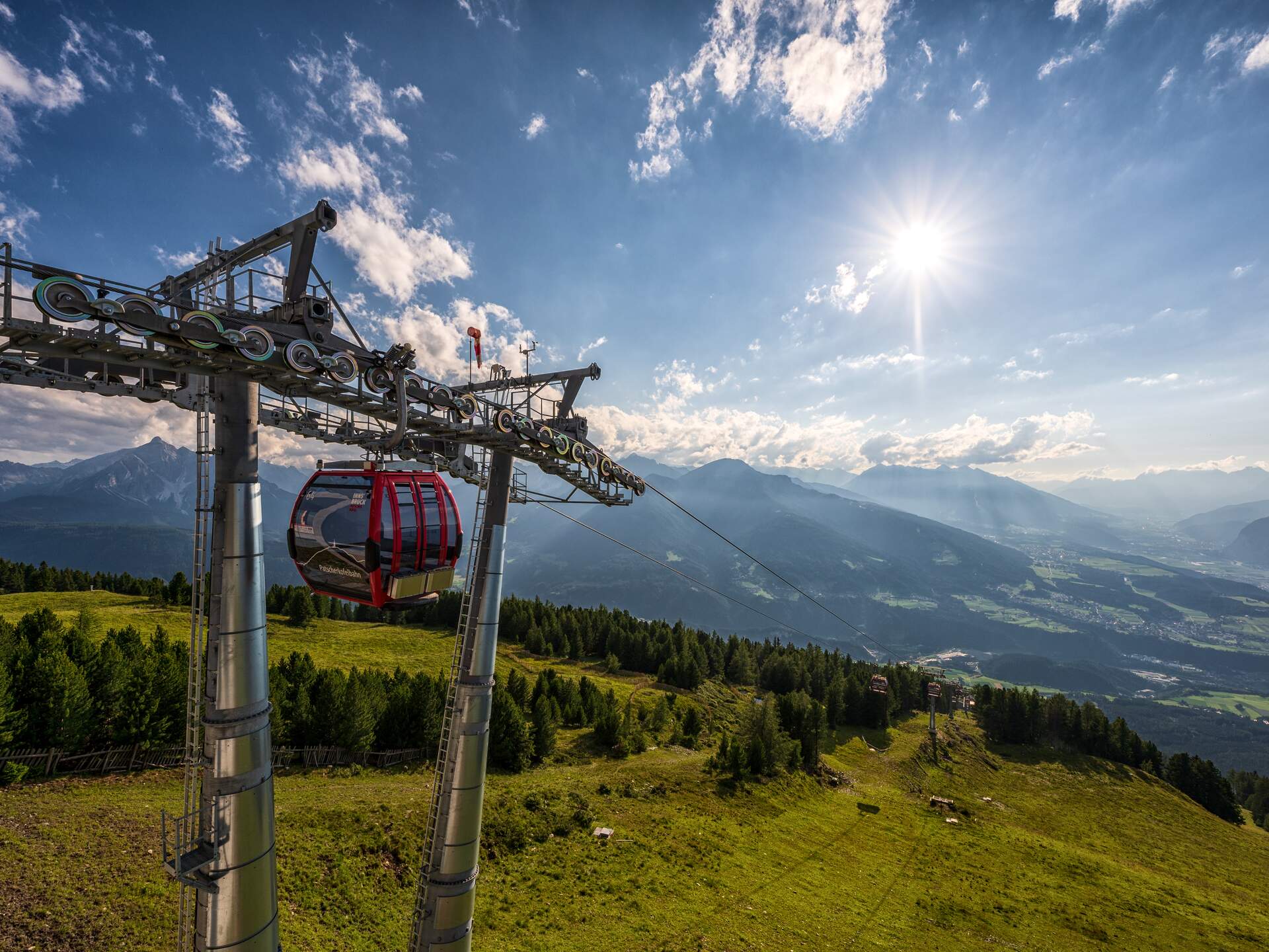 Red gondola of the Patscherkofelbahn on a steel cable in front of a mountain panorama and a blue sky with sun | © Innsbruck Tourismus, Markus Mair