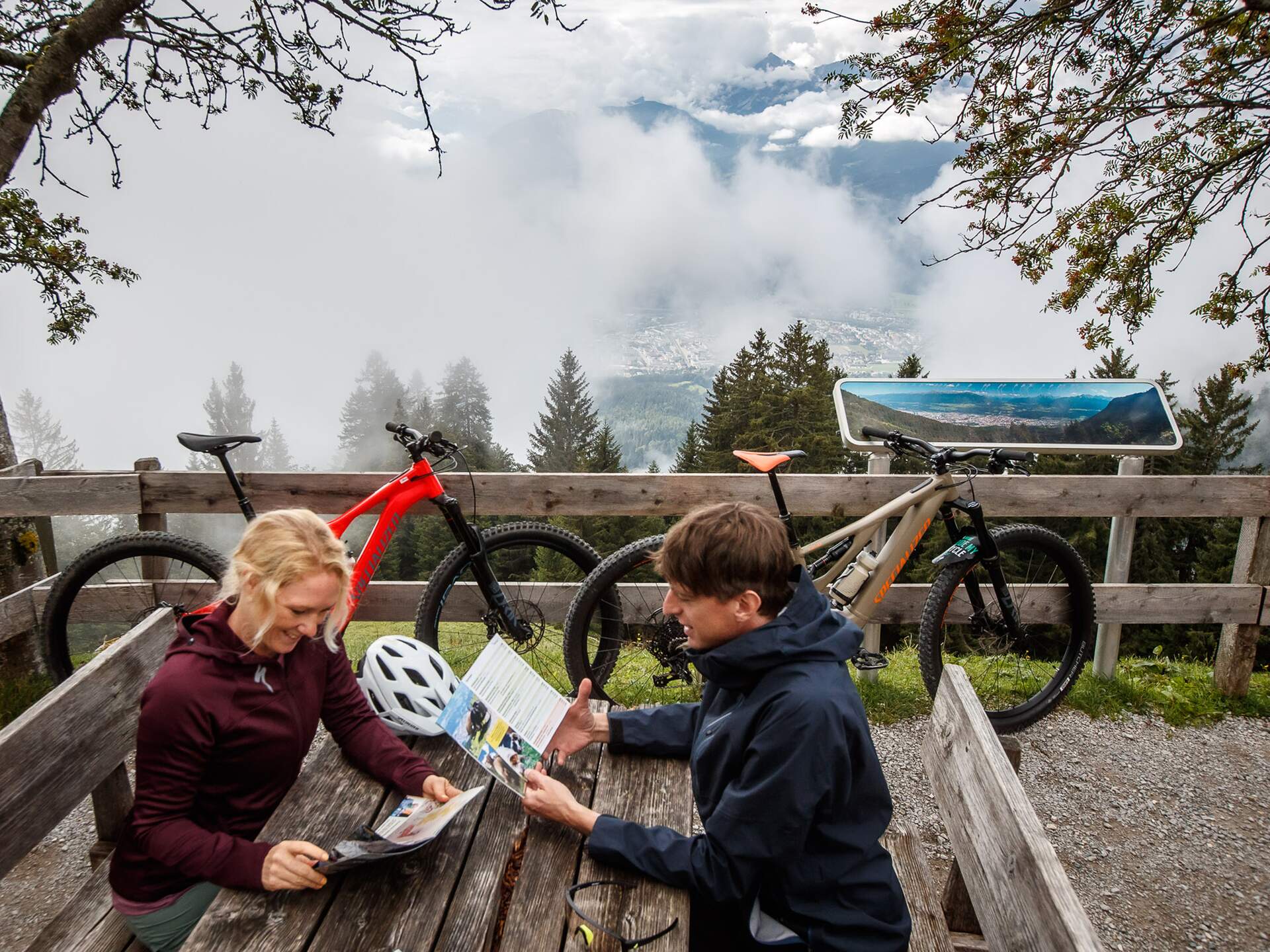 Zwei Personen mit Mountainbikes betrachten eine Karte vor Bergpanorama mit Wolken | © Erwin Haiden