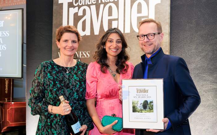 Three people proudly present an award in front of a Condé Nast Traveller banner