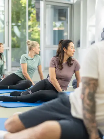 Gruppe von Menschen bei Feldenkrais-Übungen am Boden unter Anleitung eines Therapeuten