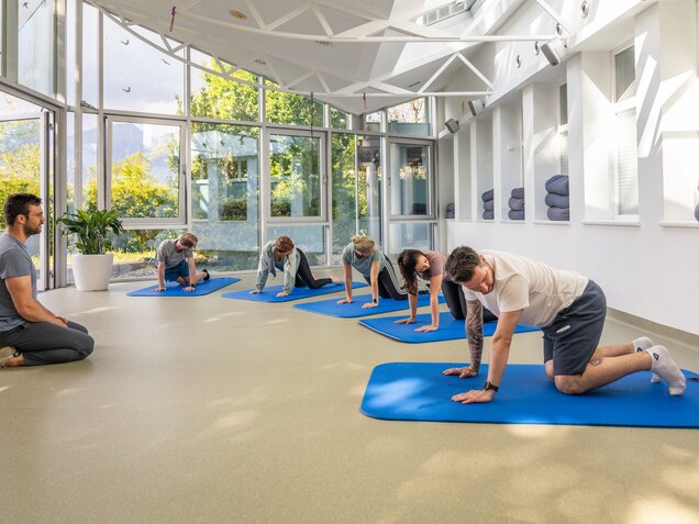 Gruppe von Menschen bei Feldenkrais-Übungen am Boden unter Anleitung eines Therapeuten