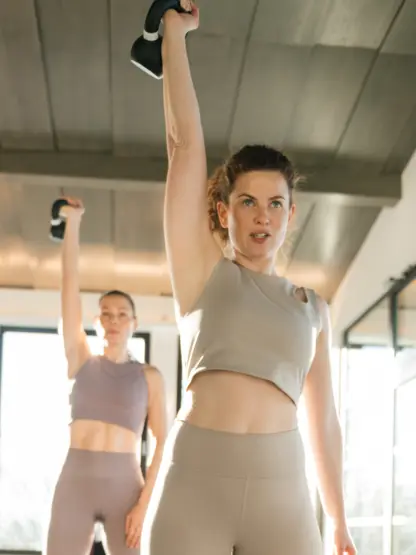Two women are working out with kettlebells in a bright gym