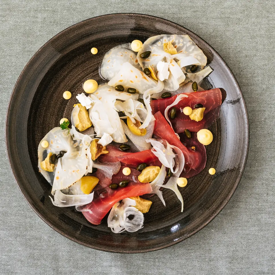 Carpaccio with fennel, capers and yellow dots on a dark plate