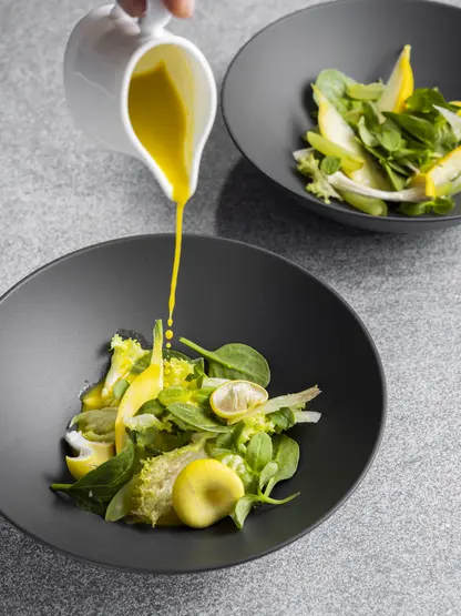 Salad in a dark bowl, dressing is poured over it