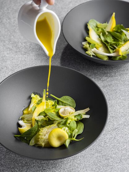 Salat in dunkler Schale, Dressing wird darüber gegossen
