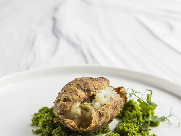 Jerusalem artichoke tartar with arugula crumbs on a white plate against a marble background