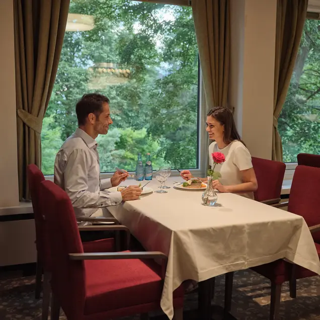 Couple eating at a set table in front of a window with a view of the greenery