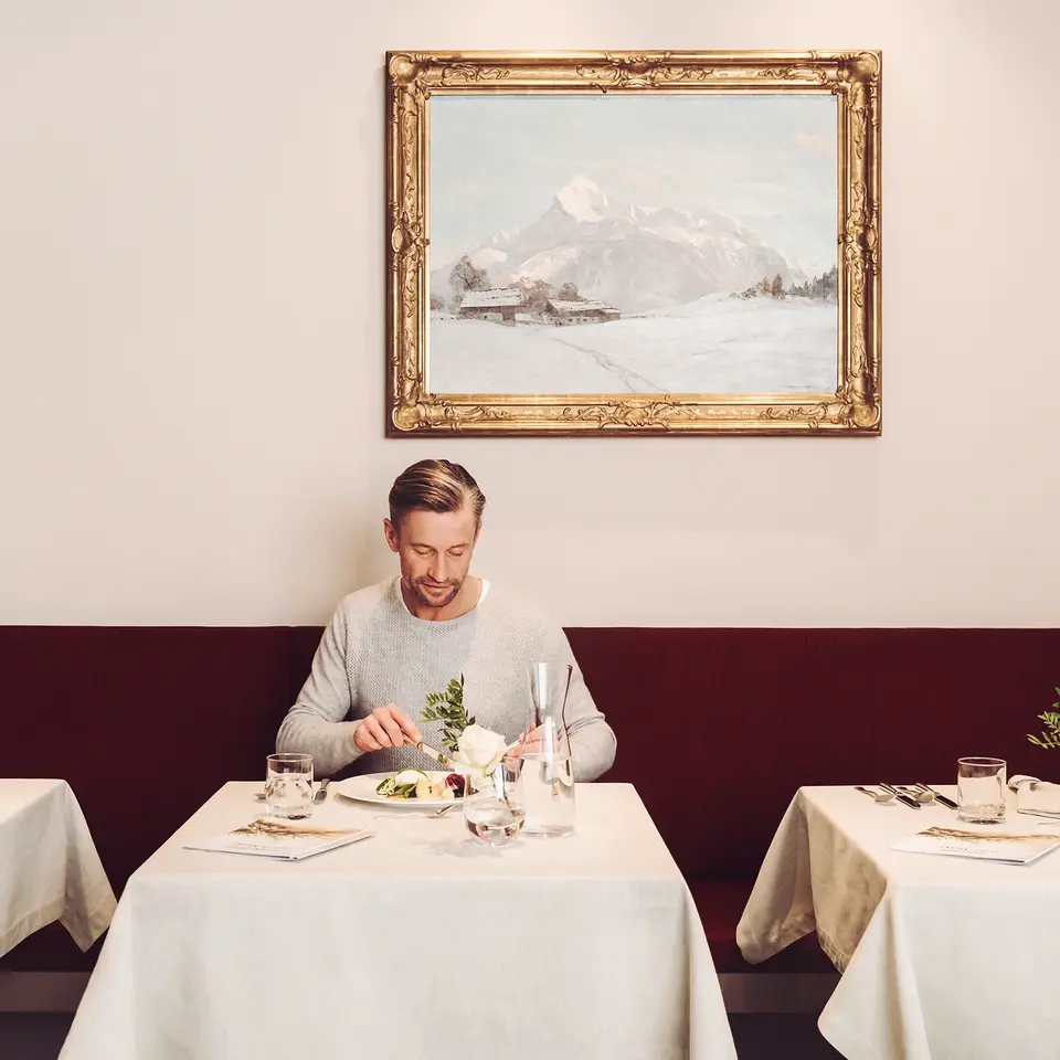 Man eating in a restaurant under a painting of a mountain landscape