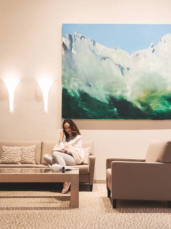 Woman sitting on sofa in lobby with painting of mountains