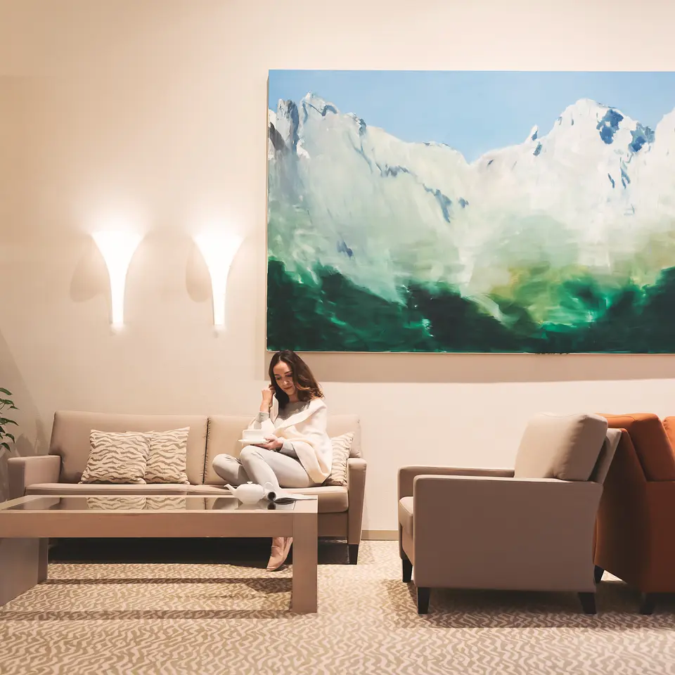 Woman sitting on sofa in lobby with painting of mountains