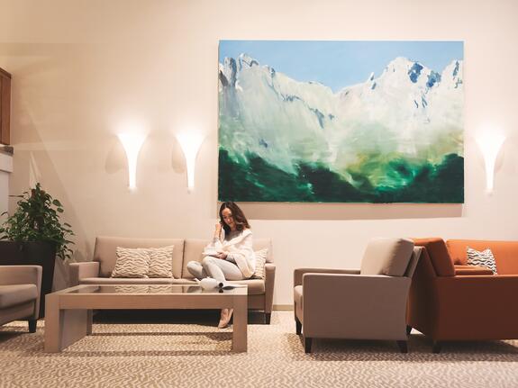 Woman sitting on sofa in lobby with painting of mountains