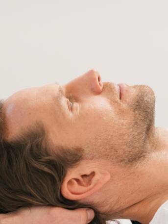 Mann erhält Nackenmassage, liegt entspannt auf weißer Liege