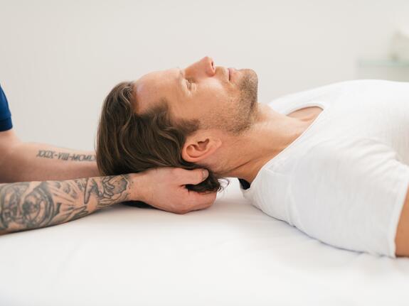 Man receiving neck massage, lying relaxed on white couch