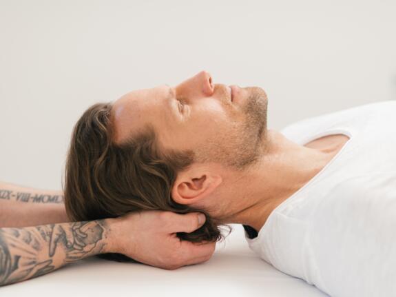 Mann erhält Nackenmassage, liegt entspannt auf weißer Liege