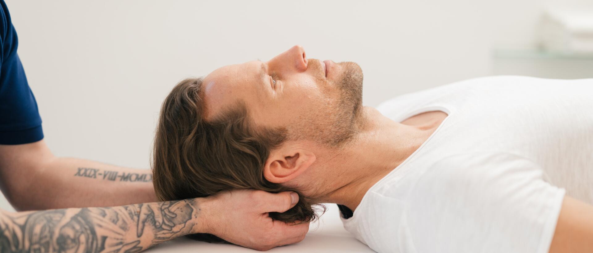 Man receiving neck massage, lying relaxed on white couch