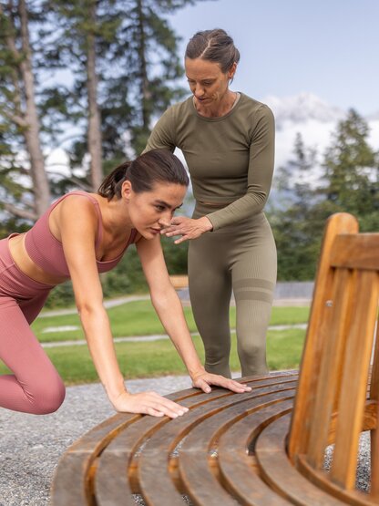 Junge Frau trainiert mit Personal Trainerin im Park an einer Bank