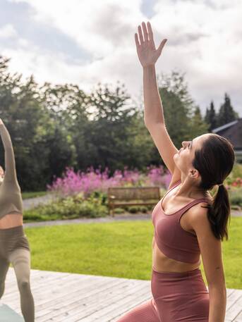 Zwei Frauen machen Yoga im Park, eine Hand erhoben