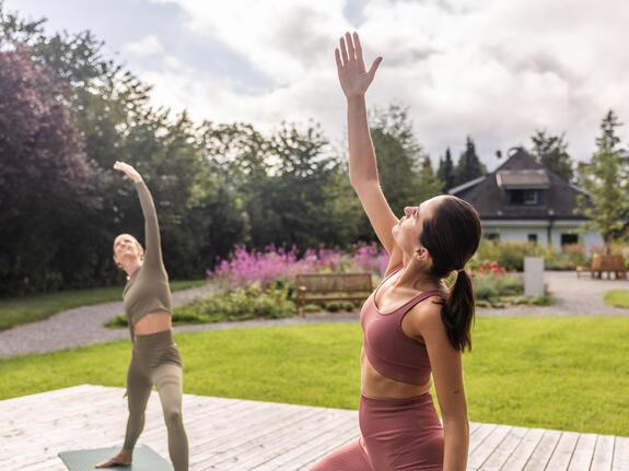 Two women doing yoga in the park, one hand raised