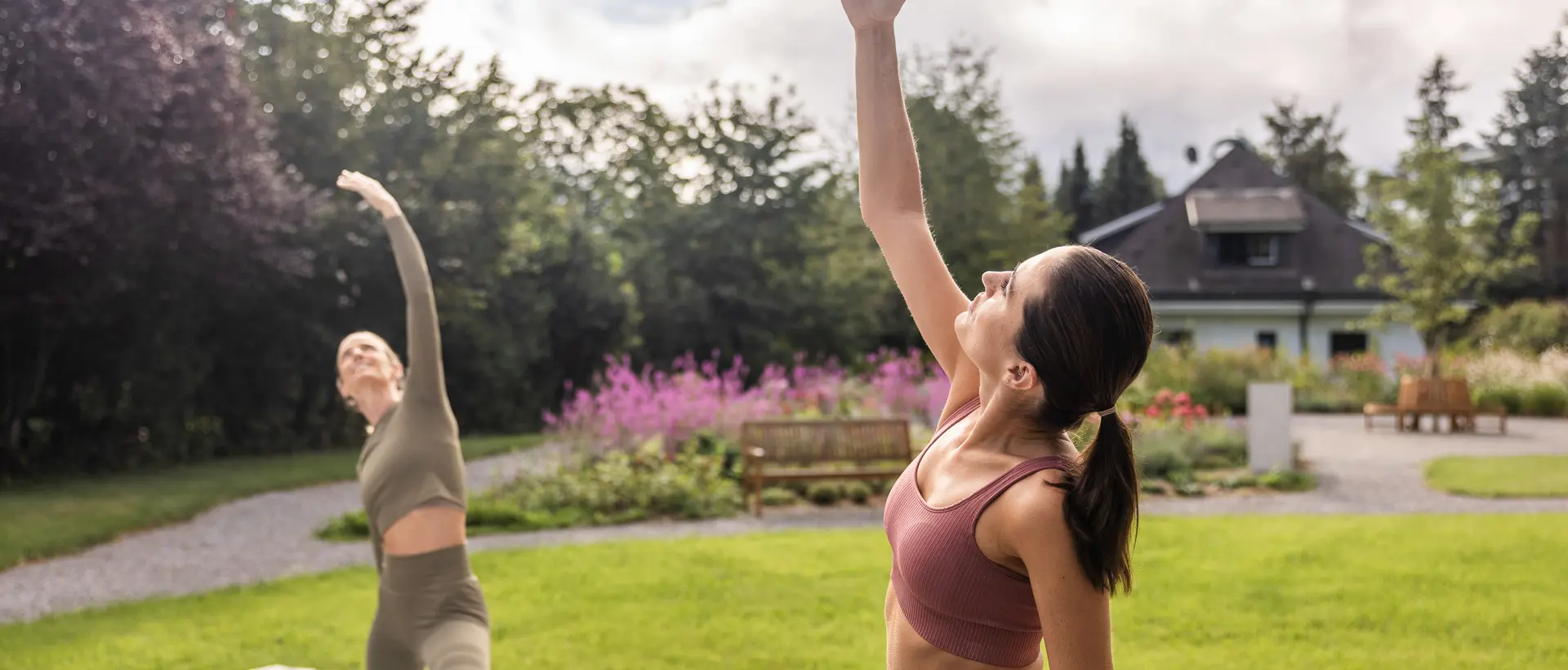 Zwei Frauen machen Yoga im Park, eine Hand erhoben