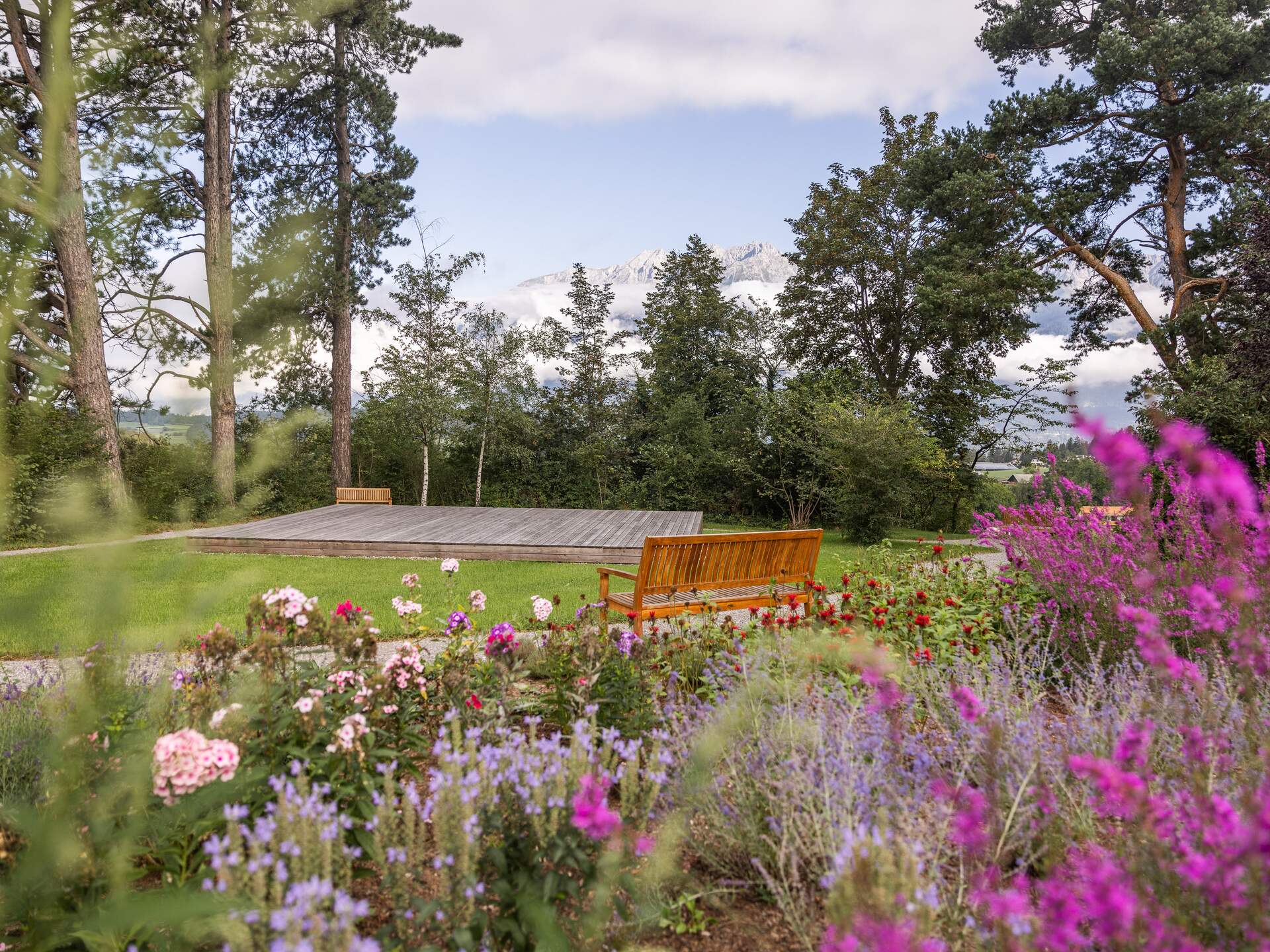 Park Igls: Blumenbeet, Rasenfläche mit Bühne und Bank vor Bäumen
