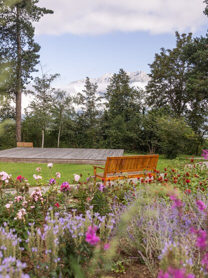 Park Igls: Blumenbeet, Rasenfläche mit Bühne und Bank vor Bäumen