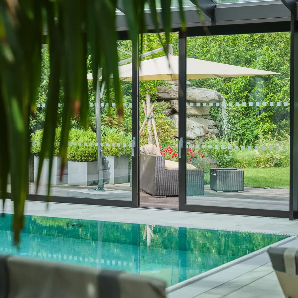Blick durch Glastür auf Garten mit Pool, Liege und Sonnenschirm