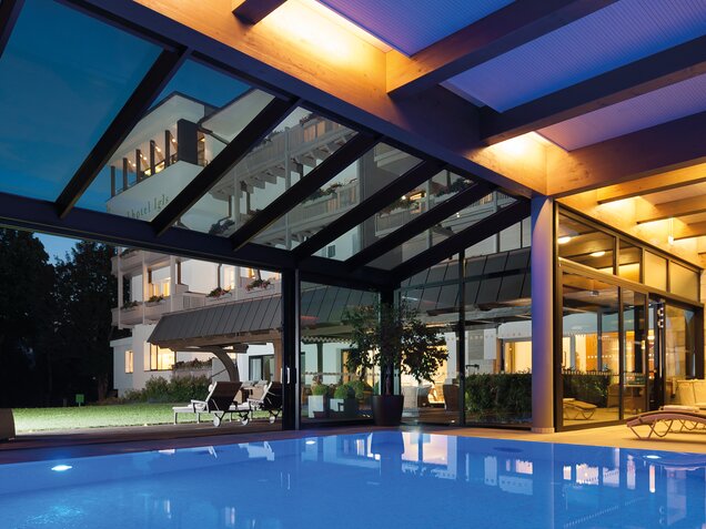 Indoor pool with glass front and view of garden with loungers at dusk