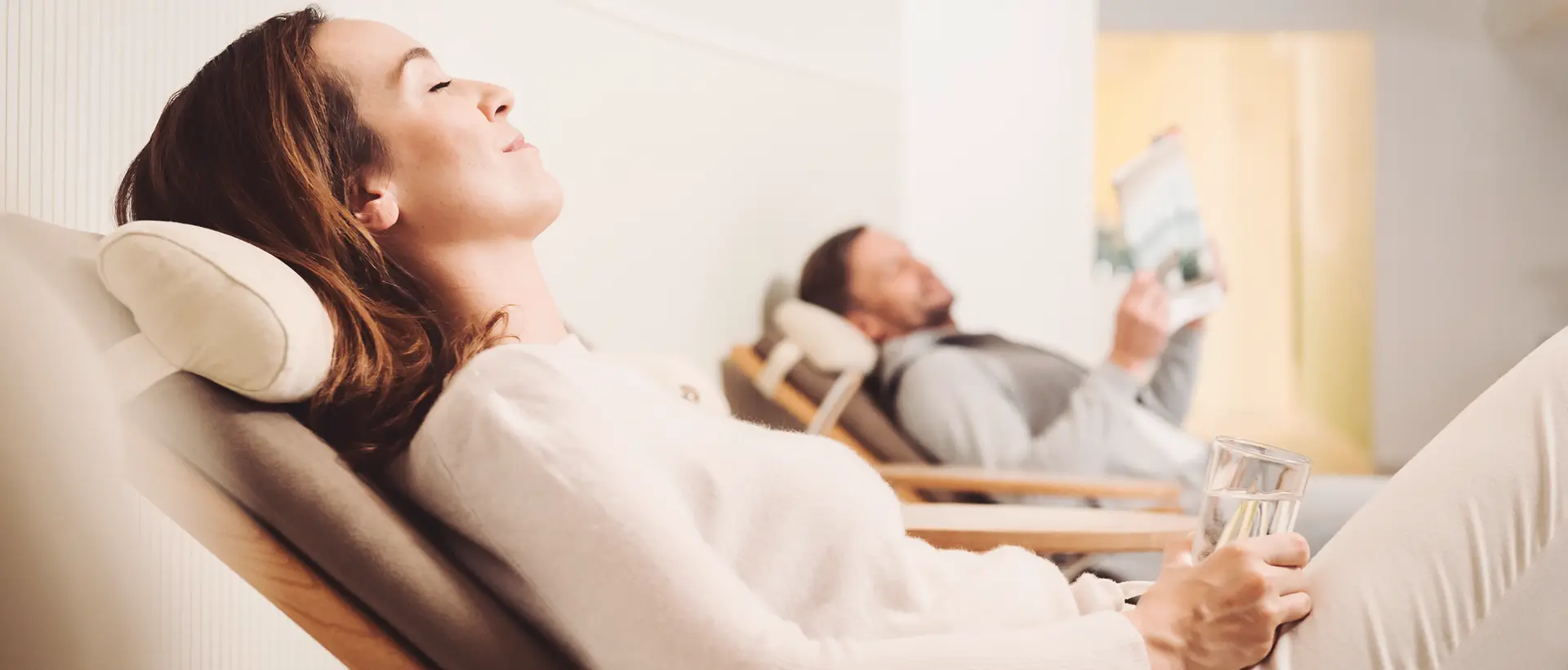 Frau und Mann entspannen in Liegestühlen im Spa, Frau mit Wasserglas, Mann mit Zeitung