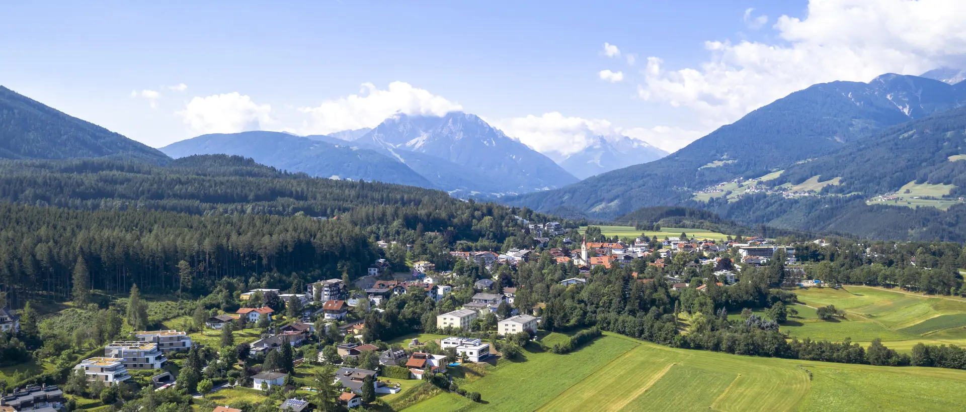 An aerial view shows Igls in summer surrounded by green meadows and forests