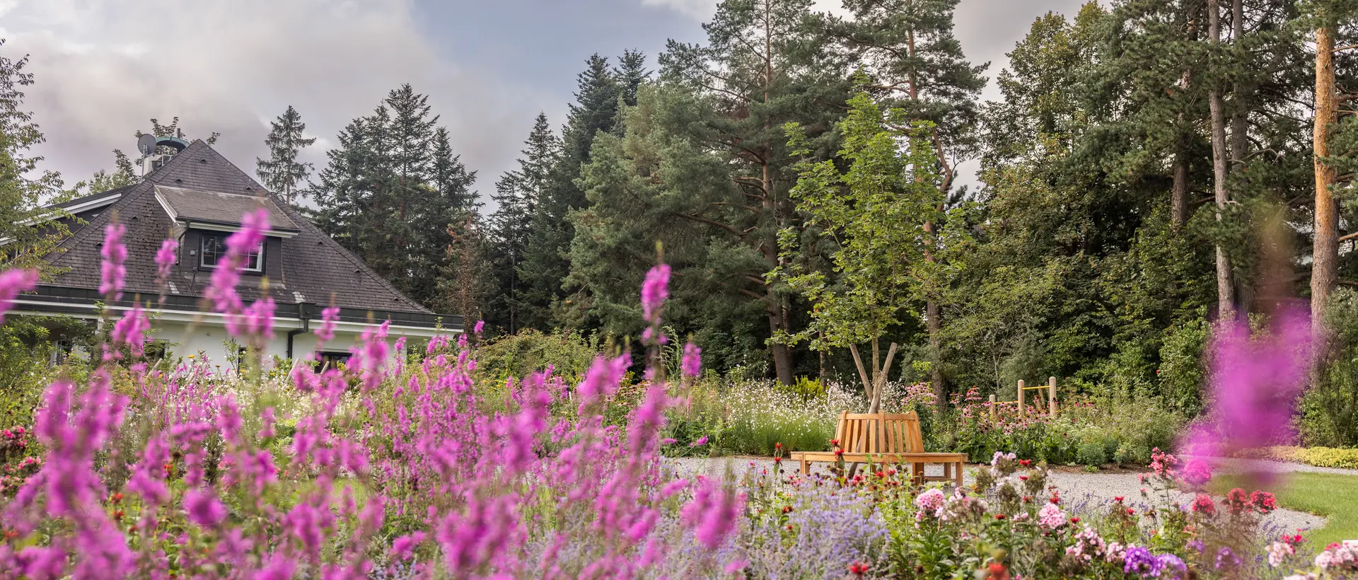 Park Igls: flowerbed, bench, trees and buildings under cloudy sky | © Blooming garden in Igls Park