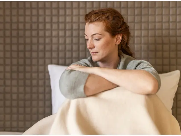 Junge Frau sitzt im Bett mit Kissen – gesunder Schlaf und Erholung im Alltag.