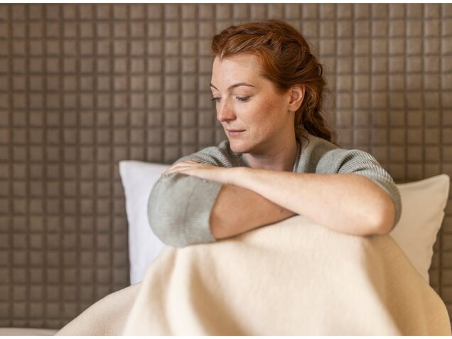 Junge Frau sitzt im Bett mit Kissen – gesunder Schlaf und Erholung im Alltag.